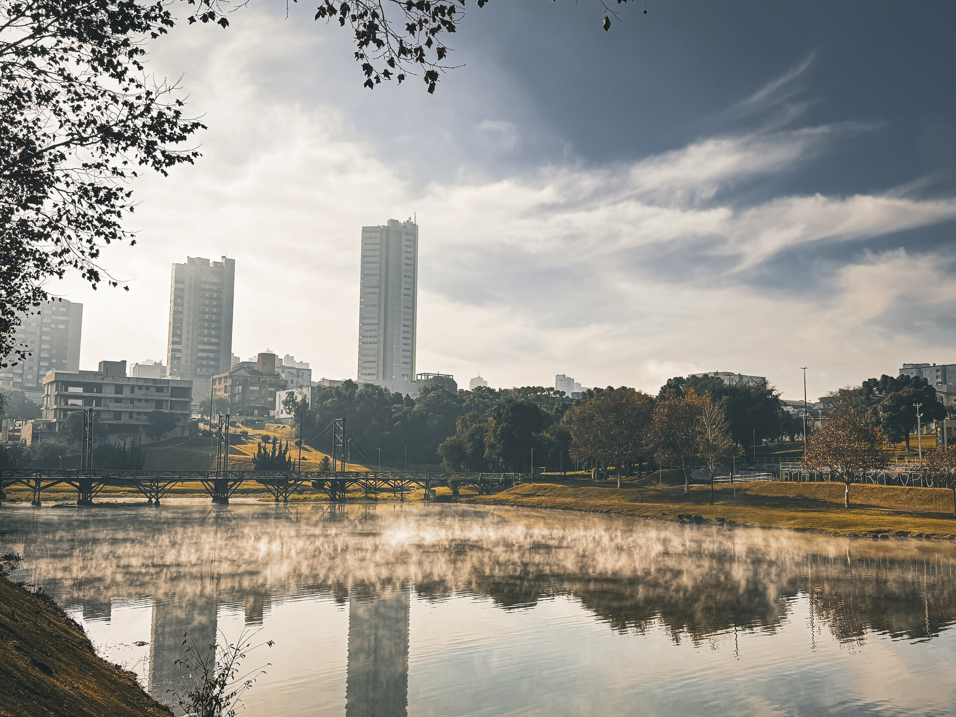 Skyline de Guarapuava ao amanhecer dourado com névoa subindo do lago