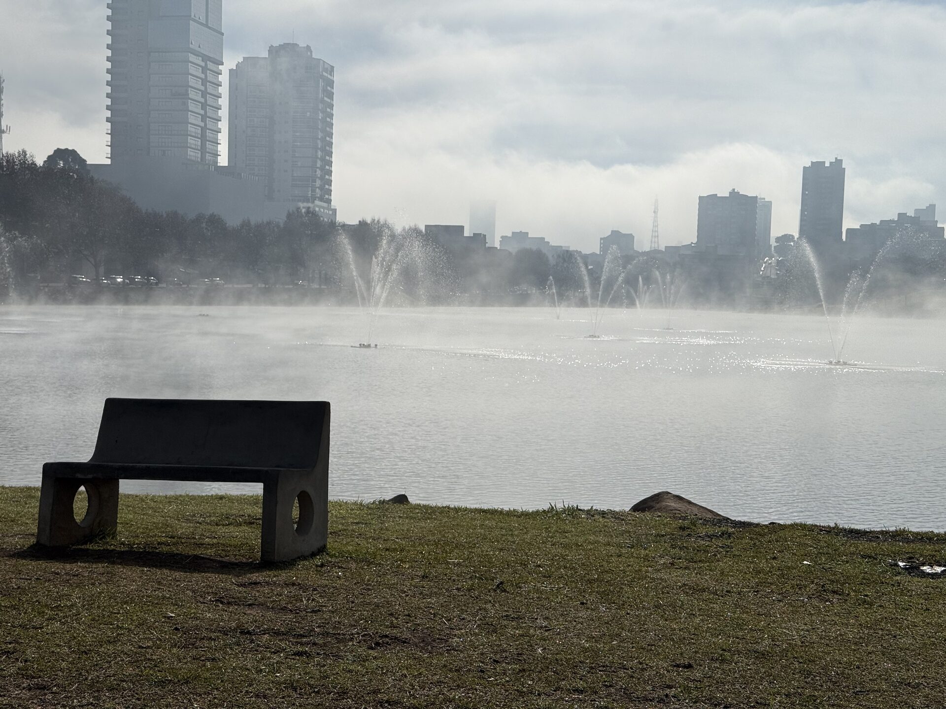 Banco à beira do lago com chafarizes e névoa de inverno